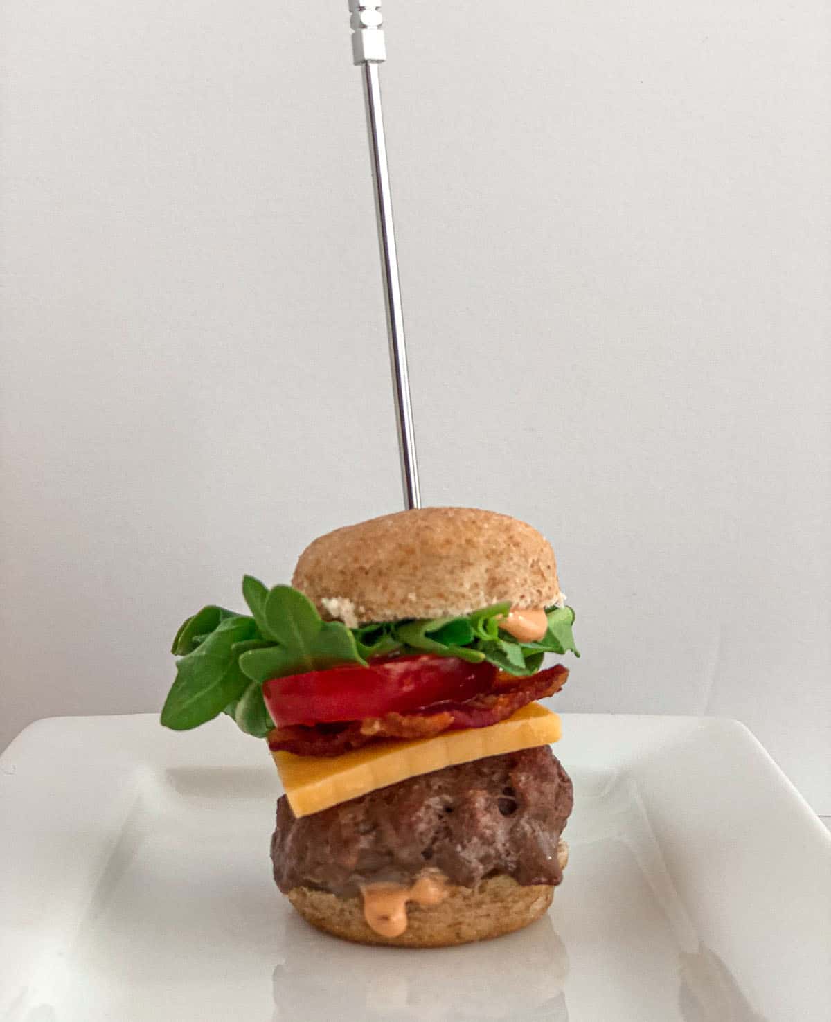 Single mini bacon cheeseburger on a white plate.