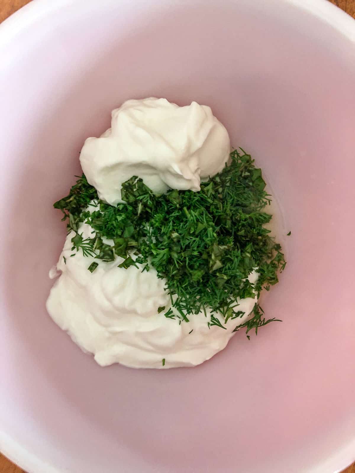 Sour cream, Greek yogurt, lemon juice, and chopped herbs in a mixing bowl.