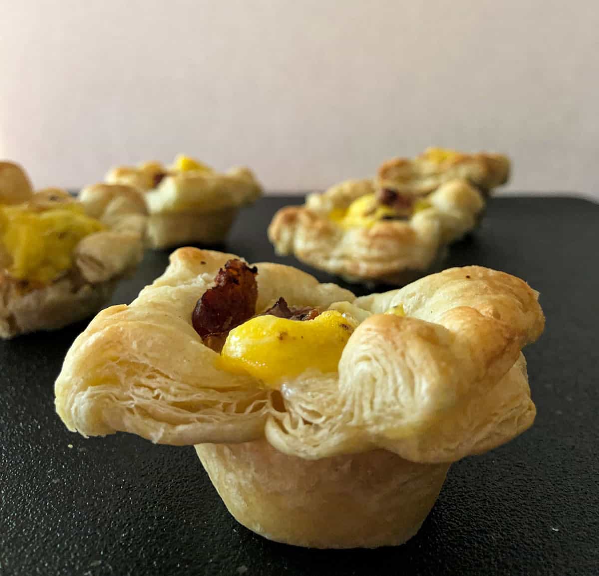 Mini puff pastry cups filled with eggs, bacon, and goat cheese.