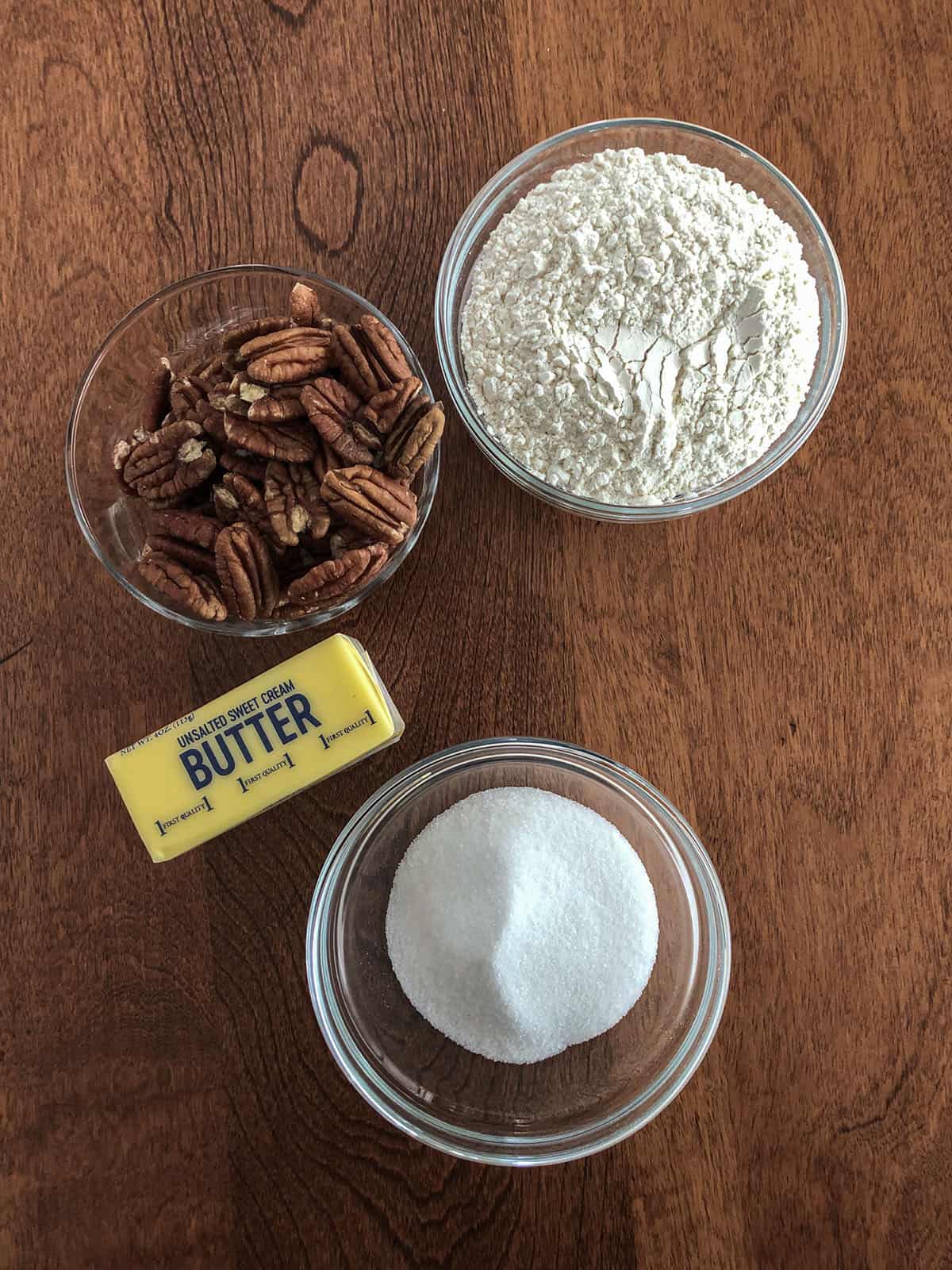 Pecans, flour, butter, and sugar in individual dishes.