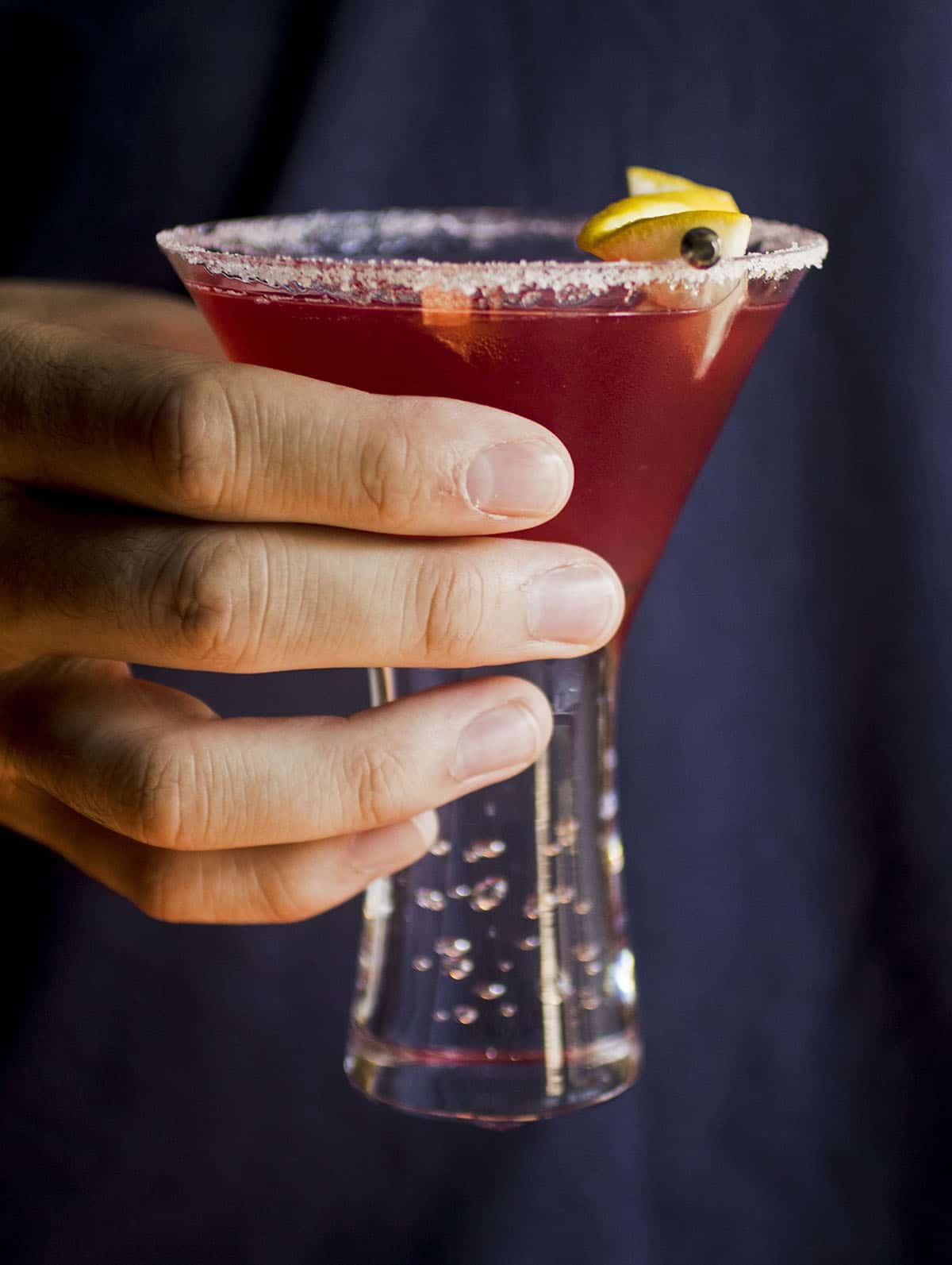 Hand holding a cocktail glass with a red drink inside.