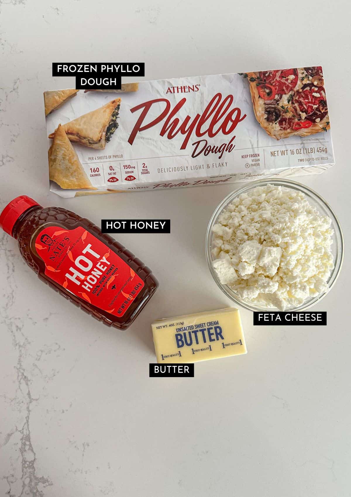 Box of phyllo dough, bottle of hot honey, crumbled feta cheese, and butter on a table top.