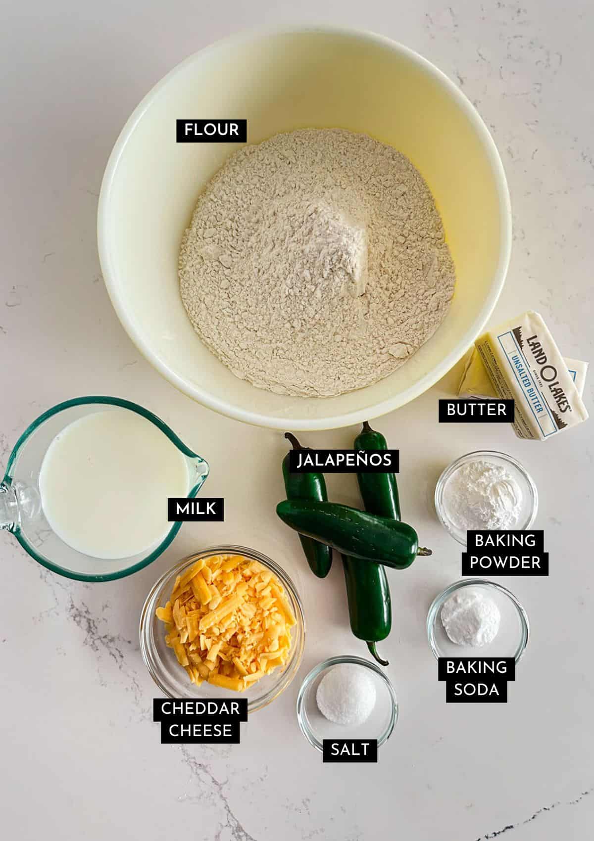Flour, milk, jalapeños, cheddar cheese, salt, baking powder and soda, and butter in individual dishes.