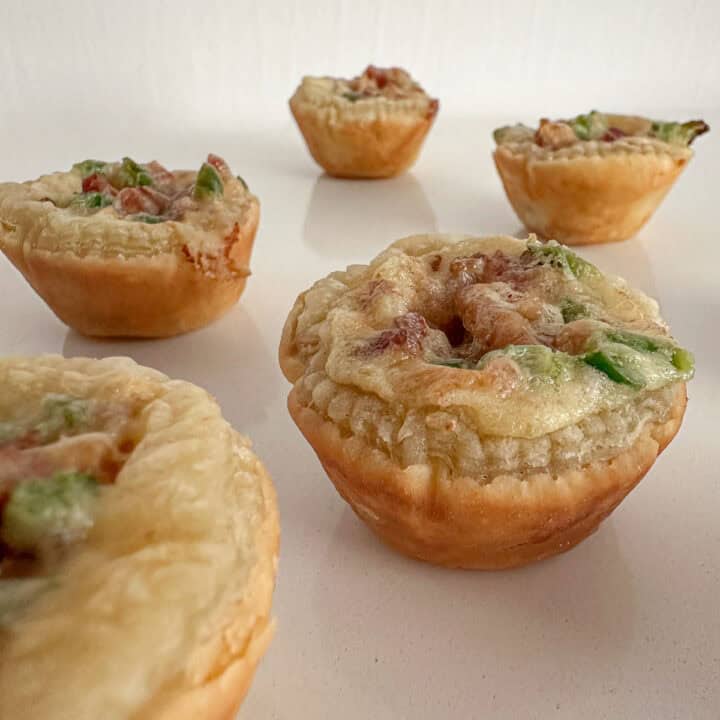 Baked mini puff pastry cups filled with cheese, bacon, and jalapeños on a counter.