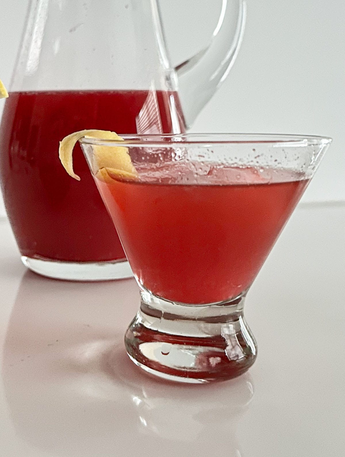 Glass with cranberry citrus cocktail and a pitcher of cranberry-citrus mix.