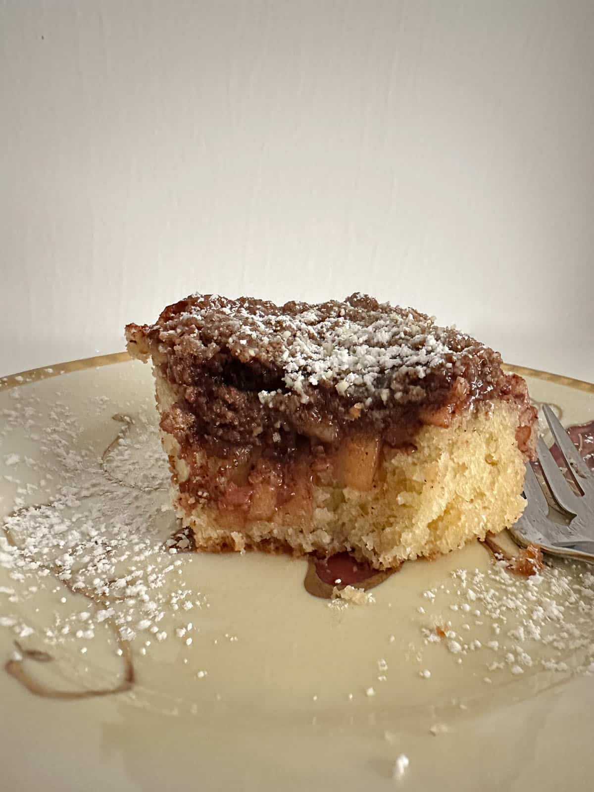 Piece of apple coffee cake on a plate with a bite gone.