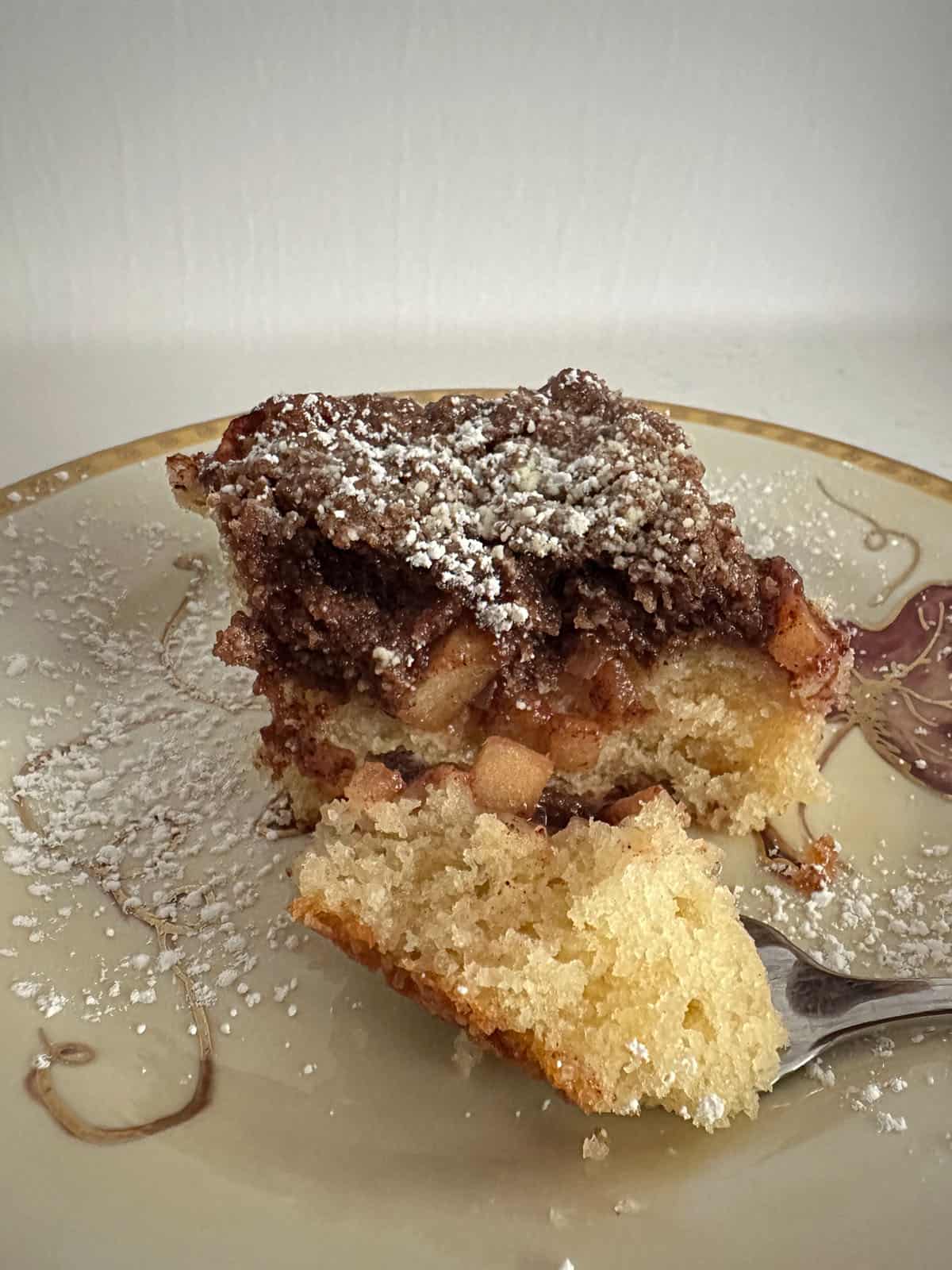 Piece of apple coffee cake on a plate with a bite on a fork.