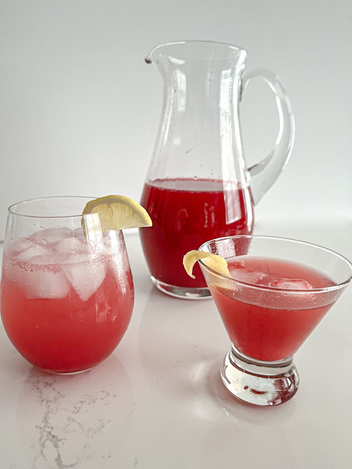 Pitcher of cranberry-citrus mix, a glass with mix and soda, and a glass with mix and whiskey.