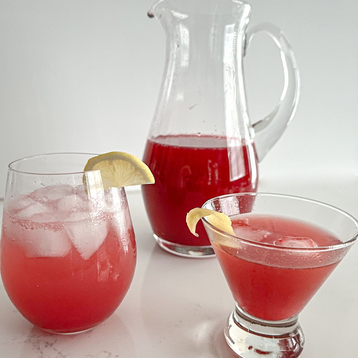 Pitcher of cranberry-citrus mix, a glass with mix and soda, and a glass with mix and whiskey.