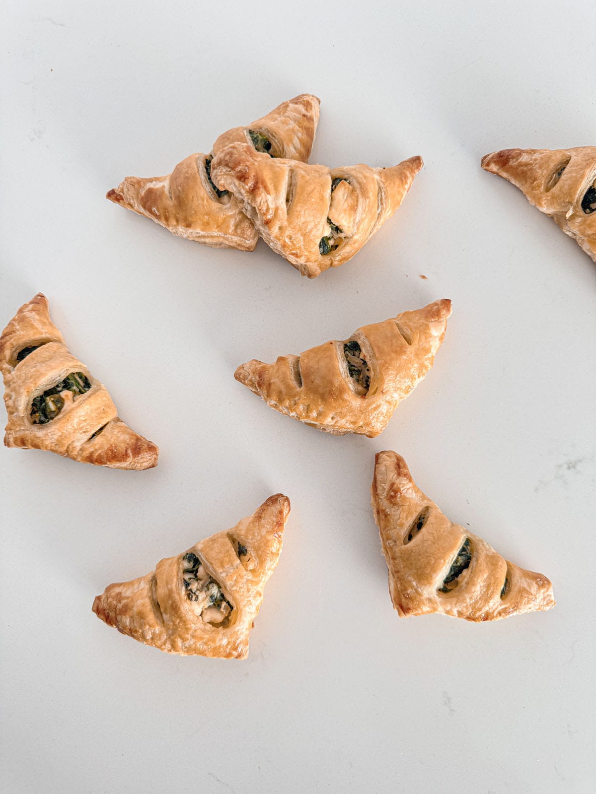 Baked spinach and feta filled puff pastry triangles on a table.
