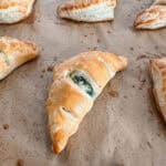 Baked puff pastry triangles filled with spinach and feta mixture on parchment paper.