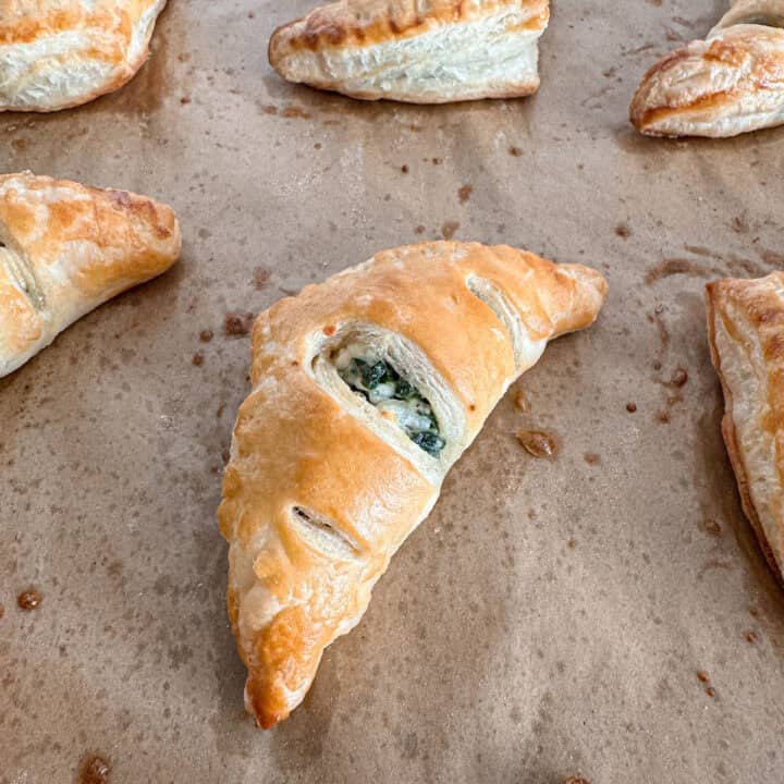 Baked puff pastry triangles filled with spinach and feta mixture on parchment paper.