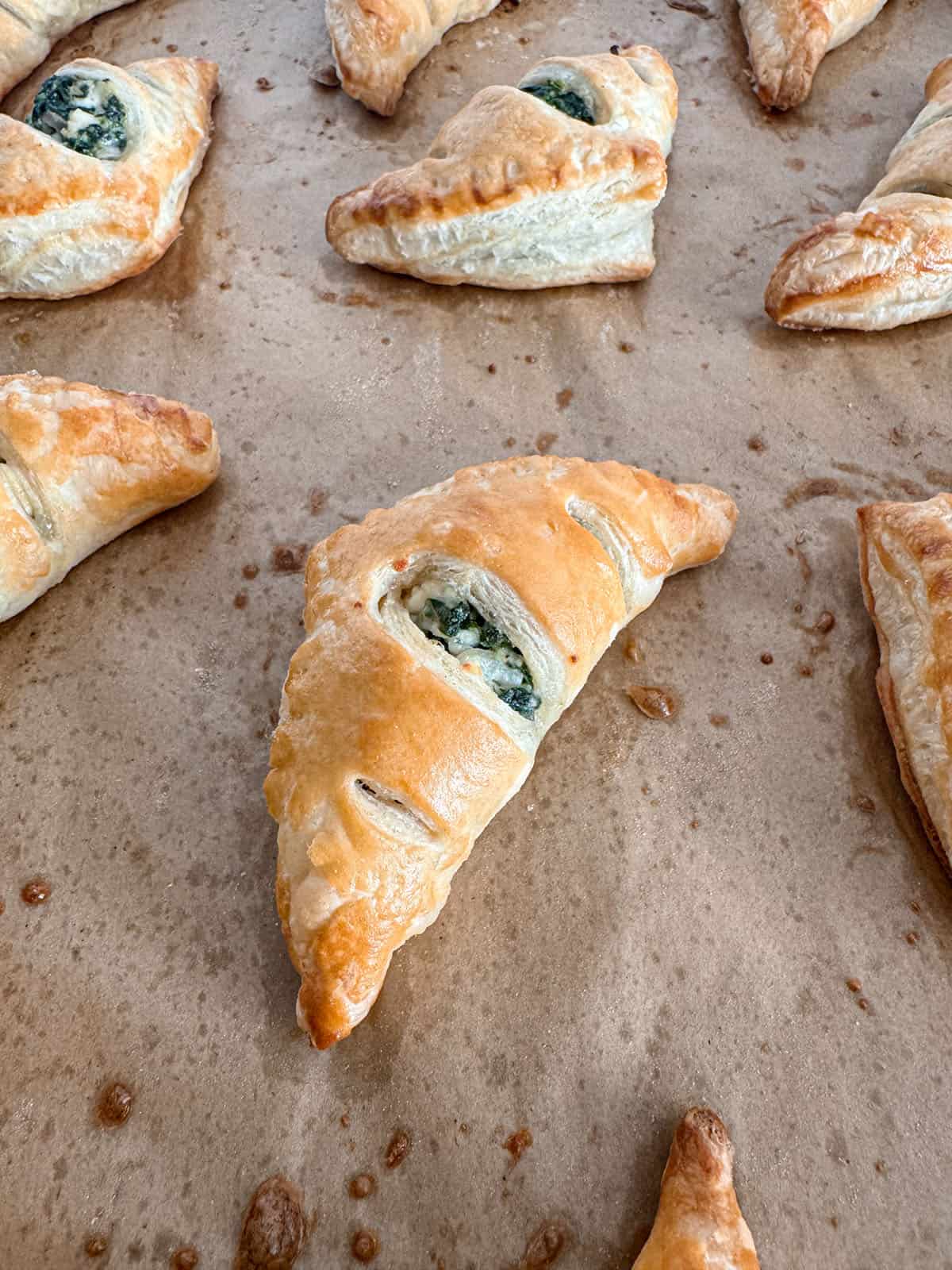 Baked puff pastry triangle filled with spinach and feta cheese mixture on parchment paper.