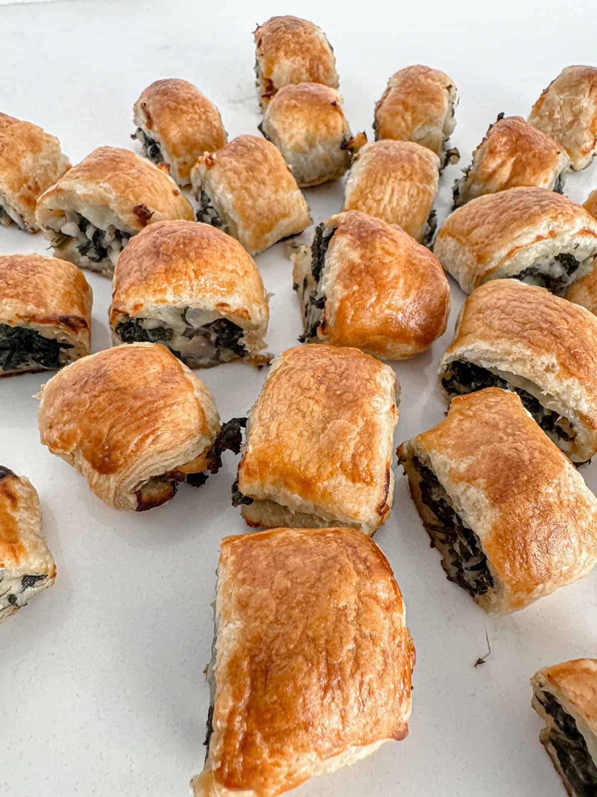 Bite-sized puff pastry filled with spinach and feta cheese on a table.