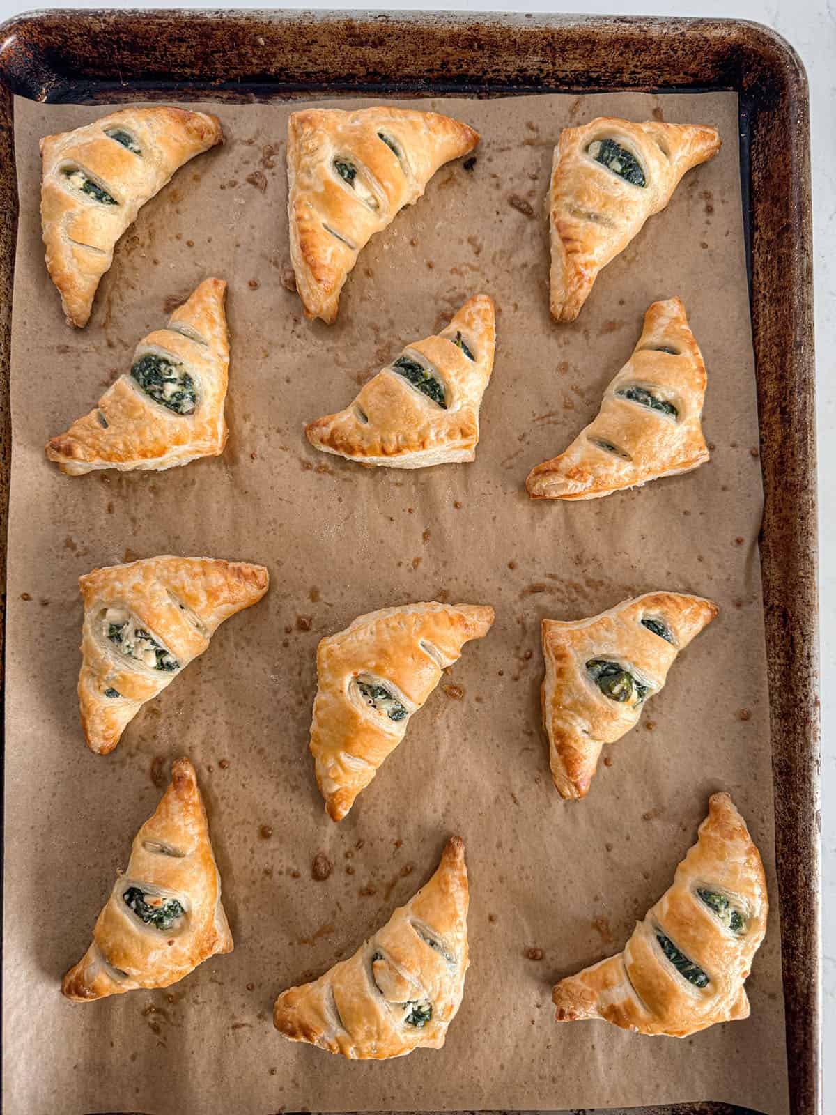 Baked spinach and feta filled puff pastry triangles on parchment lined sheet pan.