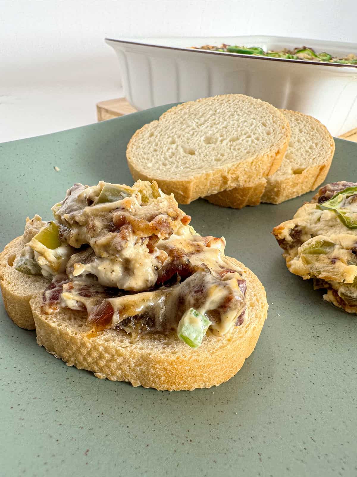 Jalapeño bacon and date dip on sliced baguette on a plate with more sliced baguette.