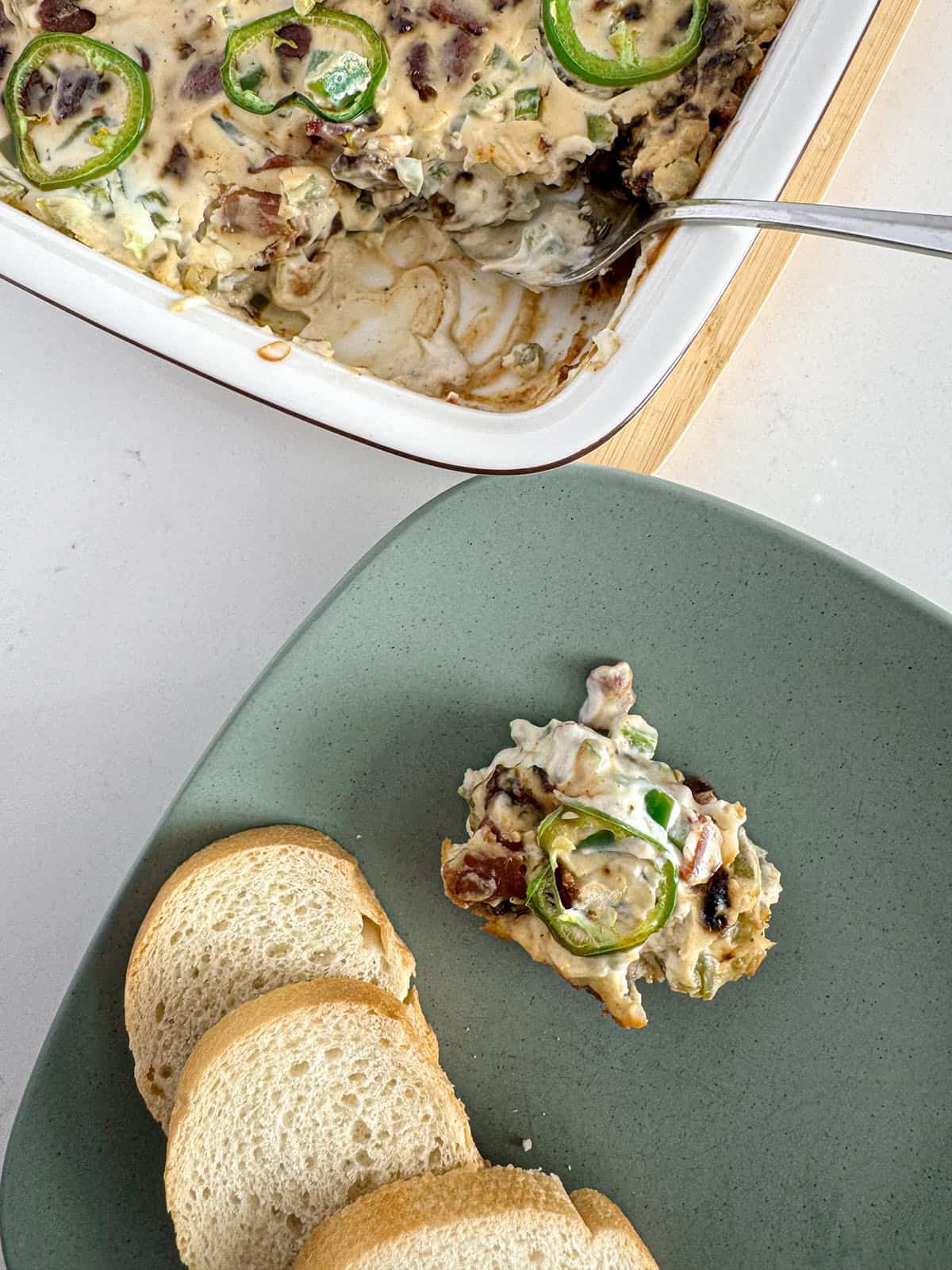 Jalapeño bacon and date dip on a plate with sliced baguette.