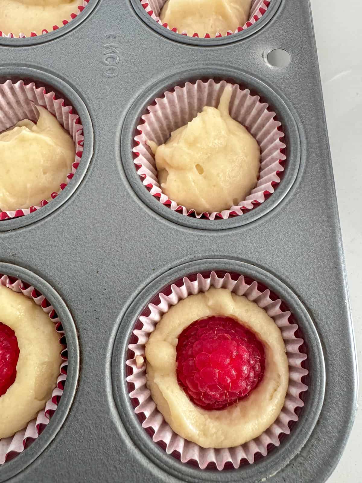 Pressing raspberry into batter filled mini muffin pan.